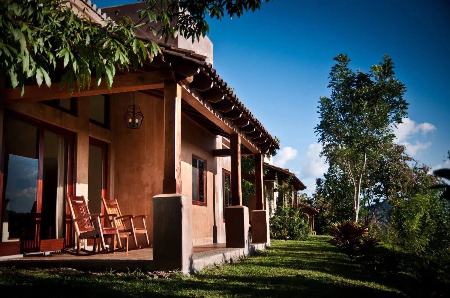 A villa's covered terrace with rocking chairs and the hills behind